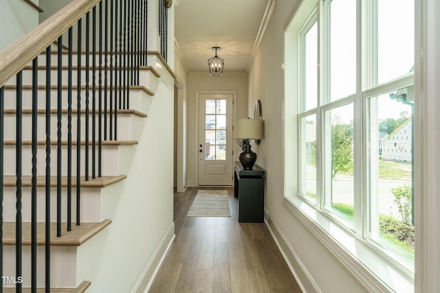 entryway with wood finished floors, a chandelier, ornamental molding, baseboards, and stairway