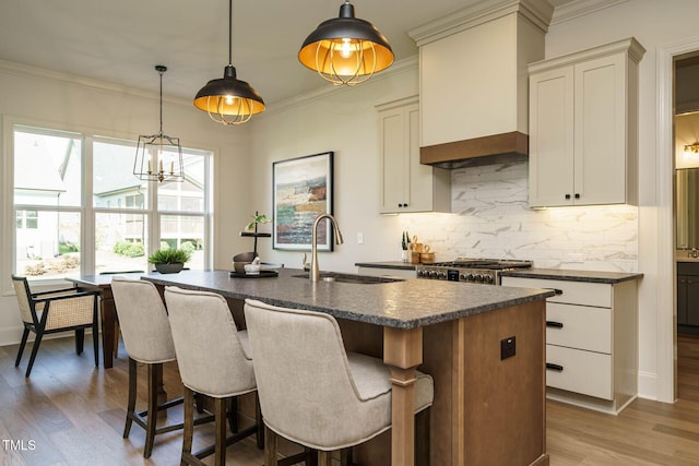 kitchen featuring dark countertops, a sink, a kitchen island with sink, and decorative backsplash