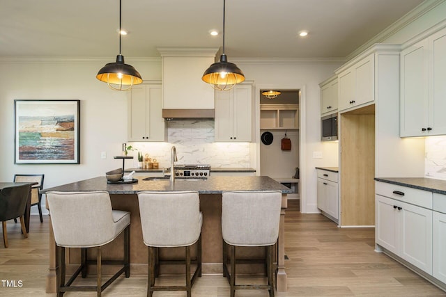 kitchen featuring tasteful backsplash, dark countertops, light wood finished floors, and a sink