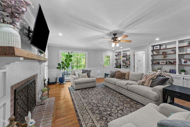2409 Beechview Ct, Raleigh, NC 27615 - living room featuring a ceiling fan, a brick fireplace, built in shelves, light wood-style floors, and ornamental molding