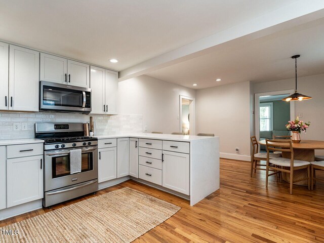 kitchen with light countertops, stainless steel appliances, a peninsula, light wood-type flooring, and backsplash