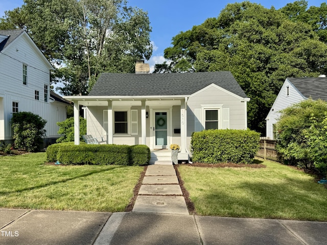bungalow featuring covered porch, a chimney, a front yard, roof with shingles, and fence