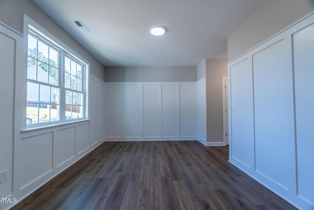 additional living space featuring visible vents, dark wood-style floors, and a decorative wall