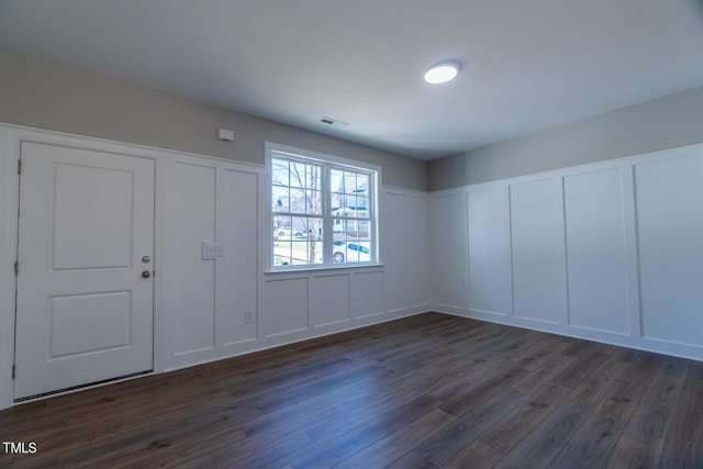 foyer featuring a decorative wall, dark wood-type flooring, and visible vents