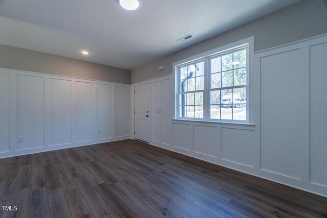 unfurnished room featuring a decorative wall, dark wood-style flooring, and visible vents