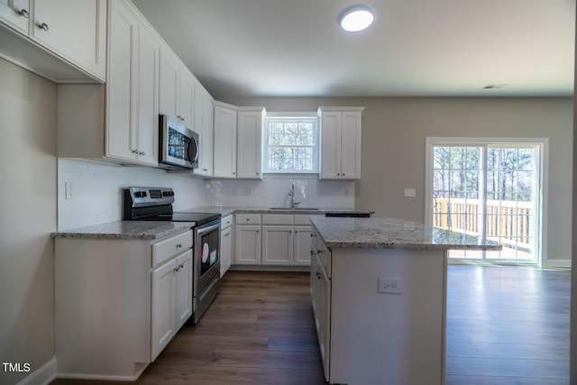 kitchen with a sink, dark wood finished floors, backsplash, appliances with stainless steel finishes, and a kitchen island