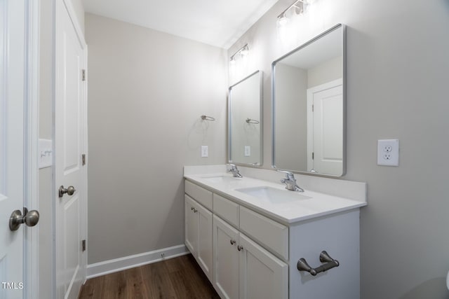 bathroom with double vanity, baseboards, wood finished floors, and a sink