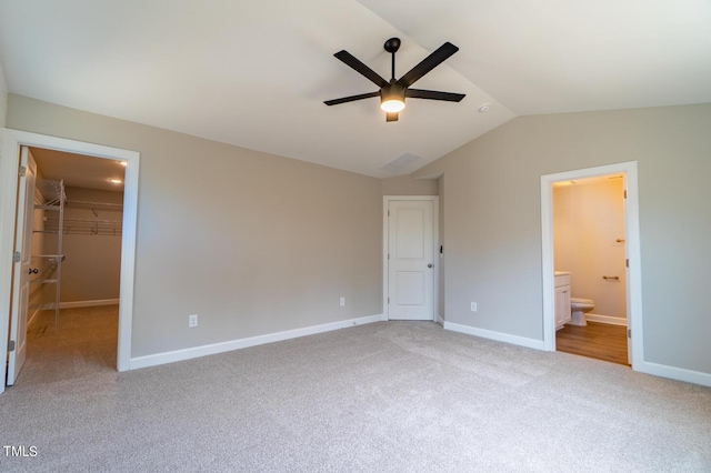 unfurnished bedroom with baseboards, a spacious closet, light colored carpet, lofted ceiling, and connected bathroom