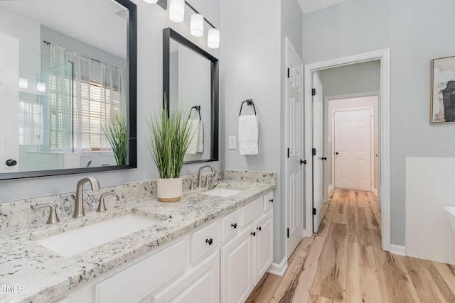 full bath with a sink, baseboards, double vanity, and wood finished floors