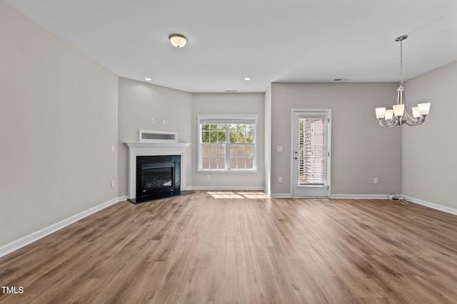 unfurnished living room with recessed lighting, wood finished floors, a chandelier, a fireplace, and baseboards