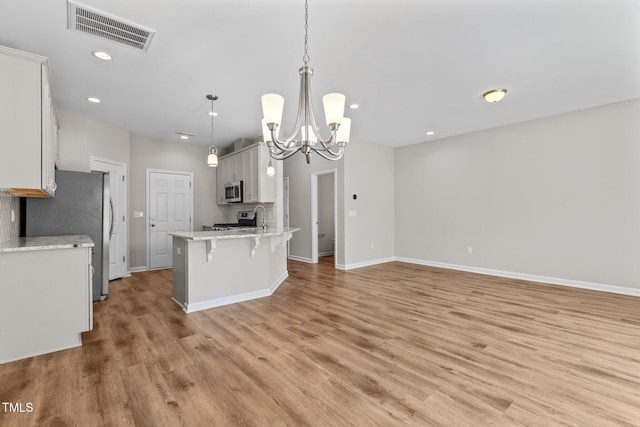 kitchen with a breakfast bar area, light wood-style flooring, visible vents, stainless steel appliances, and a chandelier