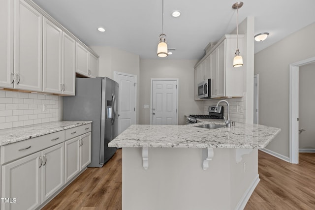kitchen featuring appliances with stainless steel finishes, backsplash, light wood finished floors, a sink, and a peninsula