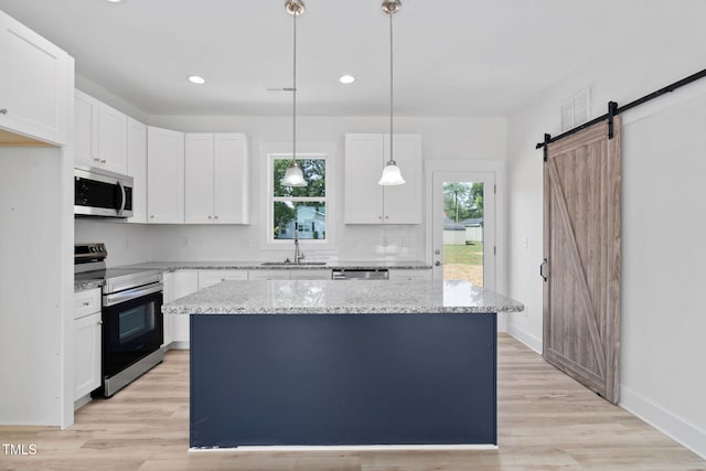 kitchen with light stone counters, a sink, white cabinetry, appliances with stainless steel finishes, and a kitchen island