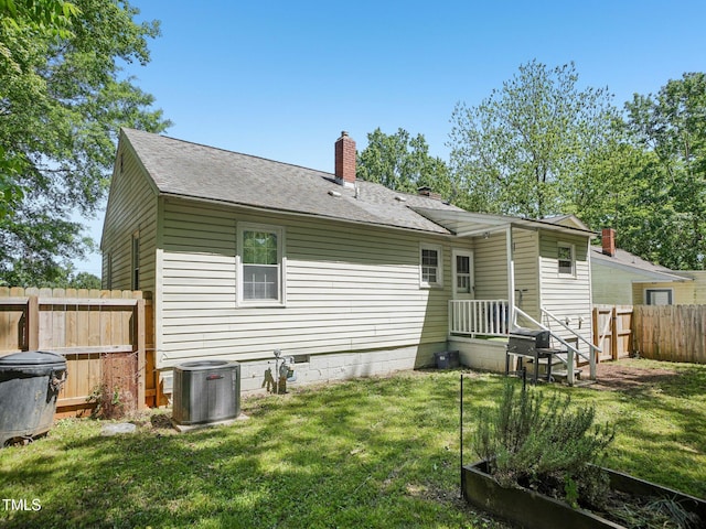 back of property with fence, a chimney, a yard, and central AC