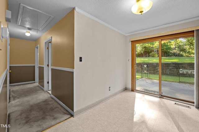 empty room with attic access, a textured ceiling, visible vents, baseboards, and ornamental molding