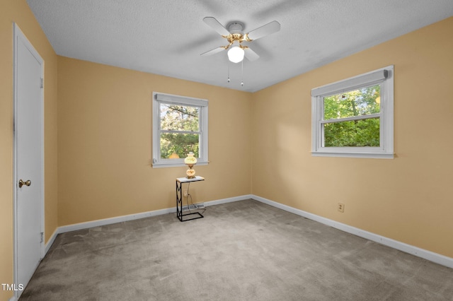 carpeted spare room with baseboards, a ceiling fan, a textured ceiling, and a healthy amount of sunlight