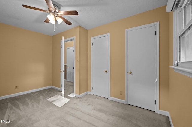 unfurnished bedroom featuring a textured ceiling, baseboards, light colored carpet, and ceiling fan