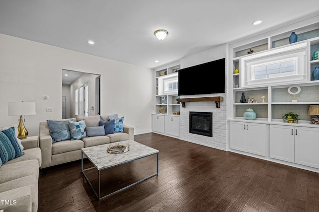 living area with built in features, a brick fireplace, baseboards, recessed lighting, and dark wood finished floors