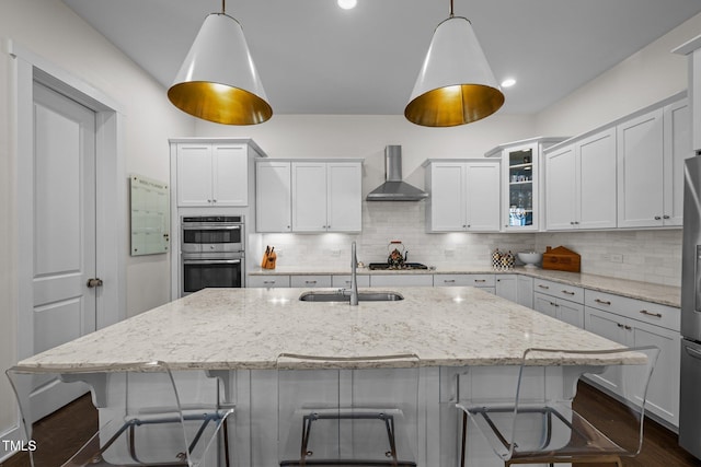 kitchen featuring stainless steel appliances, decorative backsplash, a sink, and wall chimney exhaust hood
