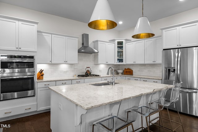 kitchen featuring wall chimney range hood, appliances with stainless steel finishes, a sink, a kitchen breakfast bar, and recessed lighting
