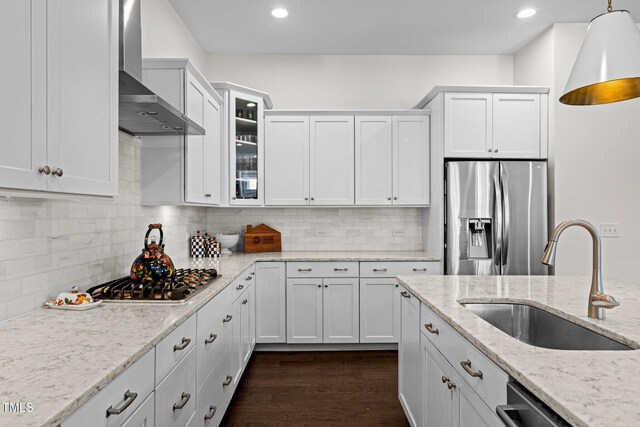 kitchen with decorative light fixtures, a sink, white cabinets, stainless steel appliances, and wall chimney exhaust hood
