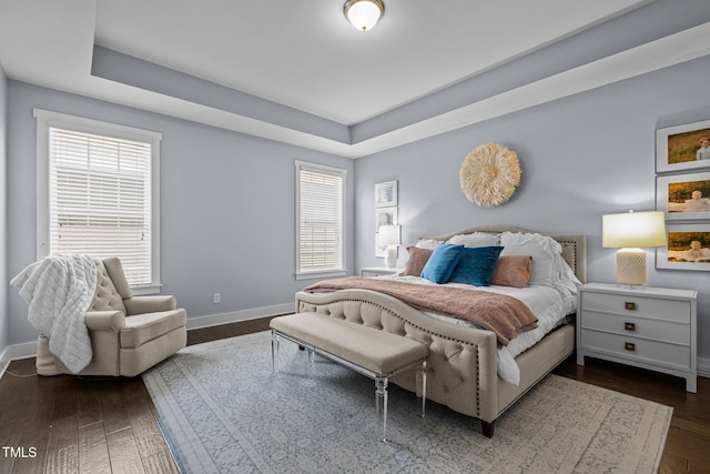 bedroom featuring baseboards, dark wood finished floors, and a raised ceiling