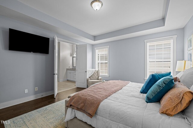 bedroom with baseboards, ensuite bathroom, and wood finished floors