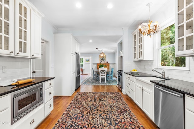 kitchen with stainless steel appliances, a chandelier, dark countertops, white cabinets, and decorative backsplash