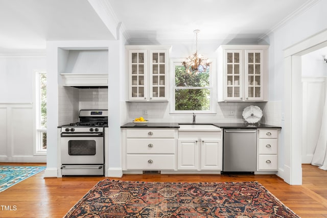 kitchen featuring appliances with stainless steel finishes, a sink, ornamental molding, dark countertops, and healthy amount of natural light