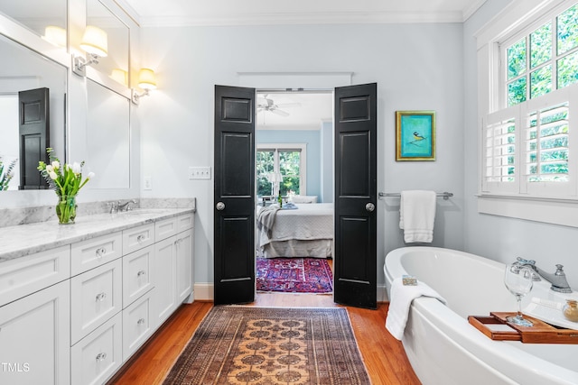 bathroom with plenty of natural light, wood finished floors, ornamental molding, vanity, and a freestanding tub
