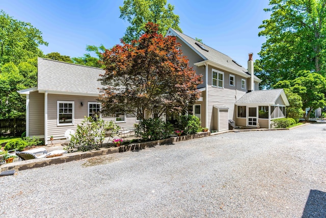 view of front facade with a sunroom, a shingled roof, driveway, and a chimney