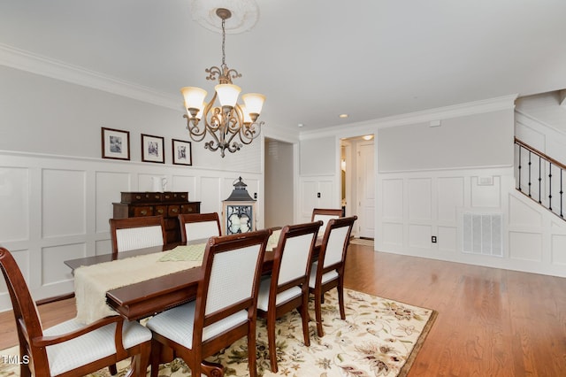 dining room featuring light wood-style flooring, a decorative wall, a chandelier, and visible vents