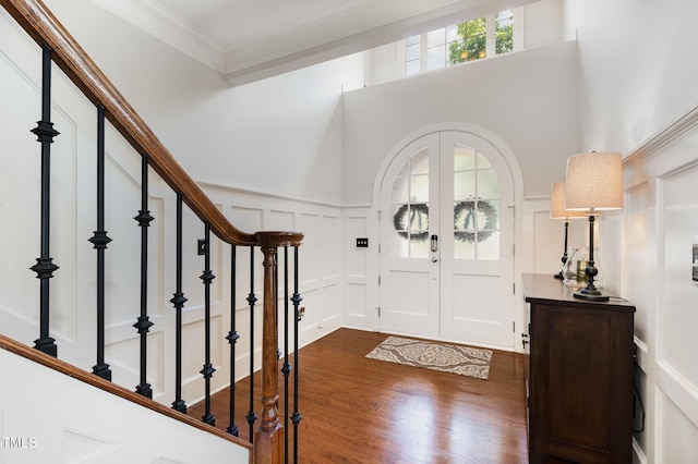 foyer entrance featuring dark wood-style flooring, crown molding, wainscoting, stairway, and a decorative wall