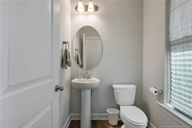 half bathroom with baseboards, wood finished floors, toilet, and a sink