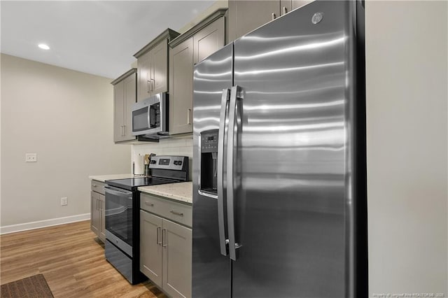 kitchen featuring light wood finished floors, backsplash, baseboards, gray cabinetry, and appliances with stainless steel finishes