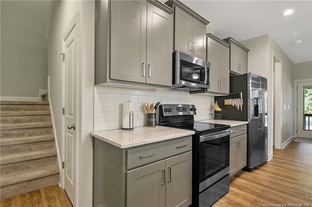 kitchen featuring tasteful backsplash, light stone counters, appliances with stainless steel finishes, light wood finished floors, and gray cabinetry
