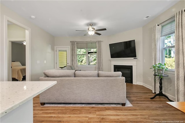 living room with light wood-style flooring, ceiling fan, a glass covered fireplace, baseboards, and visible vents
