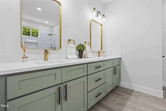 bathroom with double vanity, wood finished floors, a sink, baseboards, and a marble finish shower