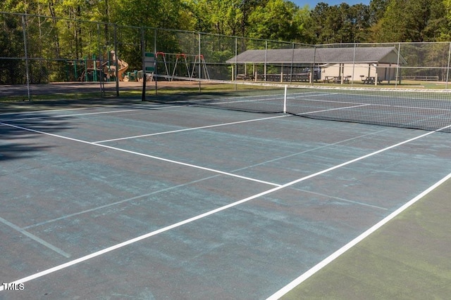 view of tennis court with fence and a wooded view