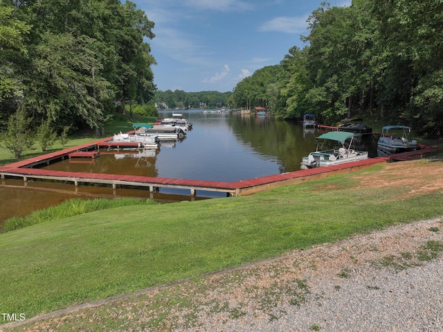 dock area with a lawn, a water view, and a view of trees
