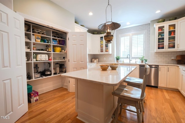 kitchen featuring white cabinets, stainless steel dishwasher, a sink, and a center island