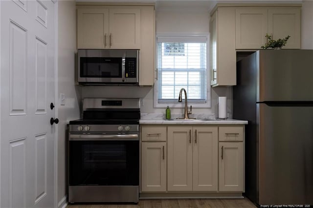 kitchen featuring a sink, light wood-type flooring, stainless steel appliances, light countertops, and ornamental molding