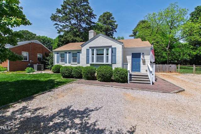 view of front facade featuring a chimney, a front yard, central air condition unit, brick siding, and fence