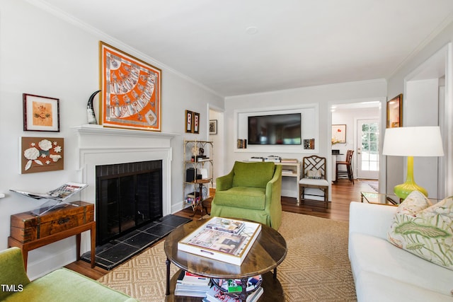 living room featuring crown molding, a fireplace with raised hearth, and wood finished floors