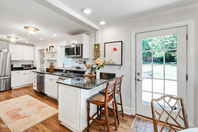 kitchen featuring crown molding, appliances with stainless steel finishes, open shelves, a sink, and a peninsula