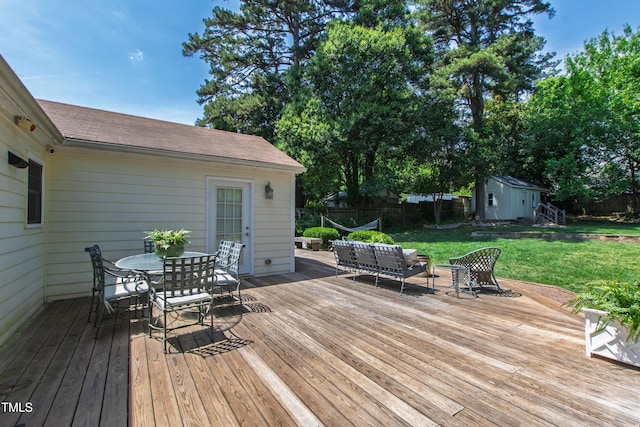 wooden deck with outdoor dining area, a lawn, a storage shed, an outbuilding, and fence