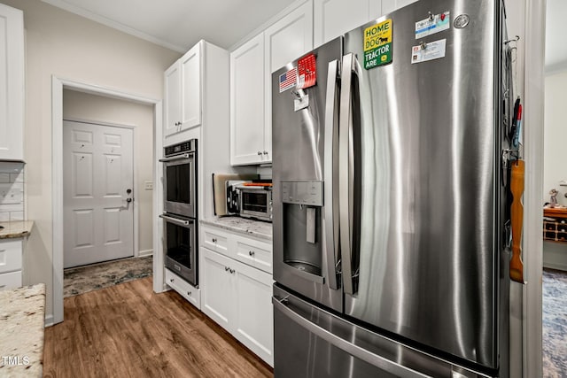 kitchen featuring wood finished floors, light stone counters, appliances with stainless steel finishes, ornamental molding, and white cabinetry