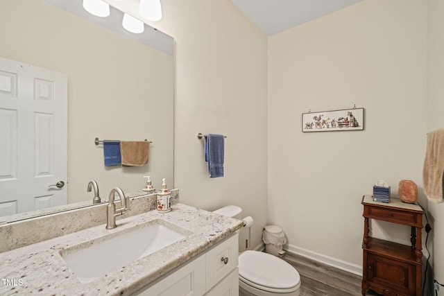 half bath featuring toilet, vanity, wood finished floors, and baseboards