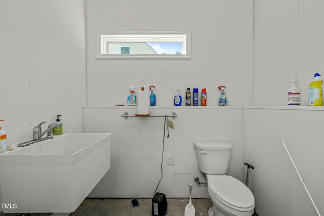 bathroom with toilet, concrete floors, and a sink