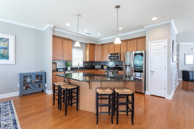 kitchen featuring appliances with stainless steel finishes, light wood finished floors, a kitchen breakfast bar, tasteful backsplash, and ornamental molding